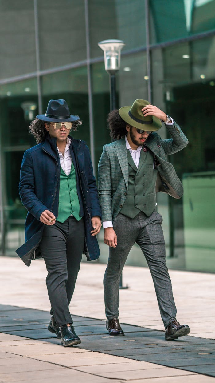 our-experience Two stylish men in suits and hats walking in an urban setting, exuding elegance and confidence.